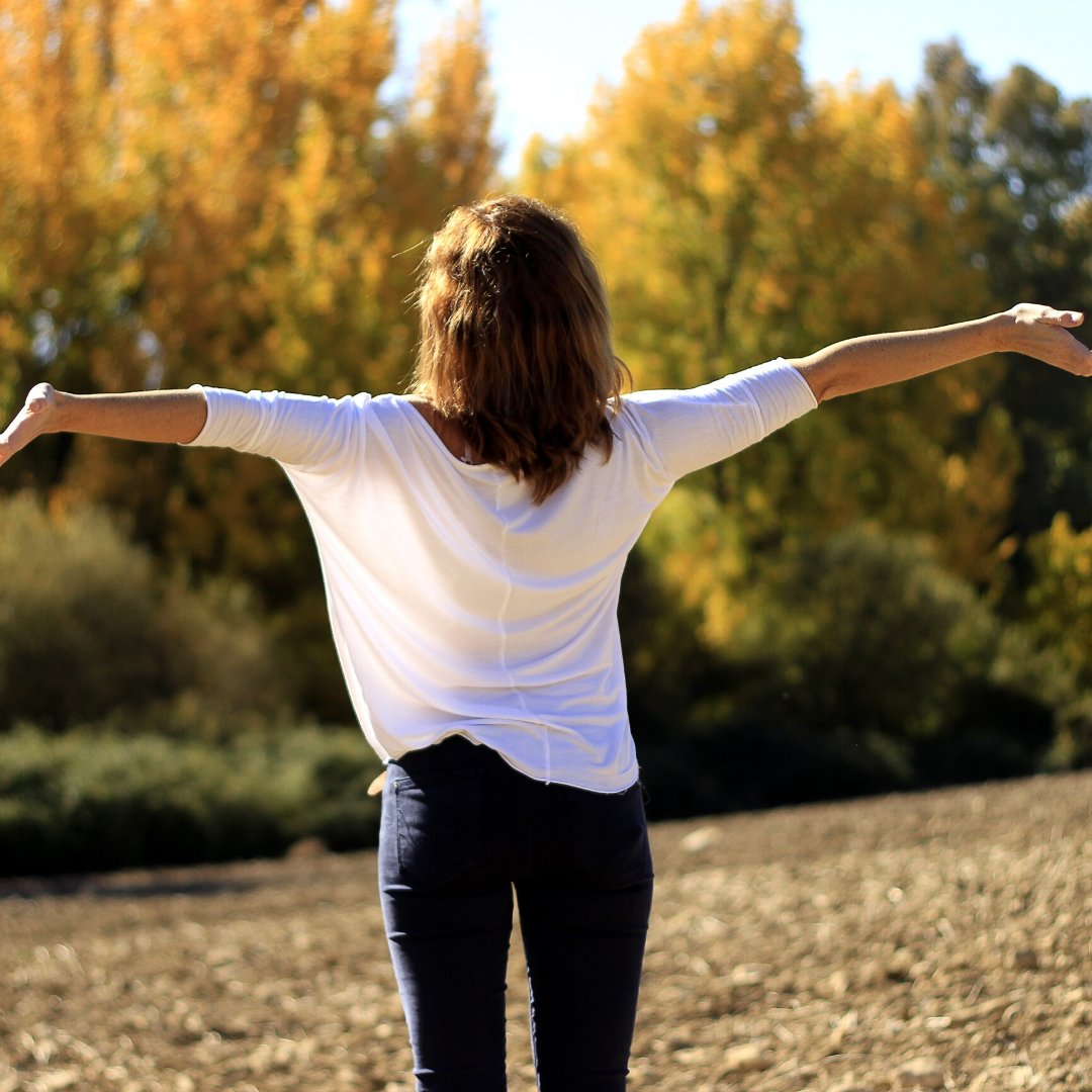 A woman with arms outstretched facing autumn trees, embracing wellness